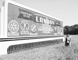 Billboard in field says A Good Place to Live London, Ontario The Forest City. A man and woman look at the sign.