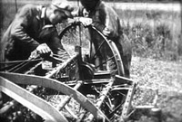 Two men fixing farm equipment. Black and white still from Massecar film, 1947-1949, location unknown.